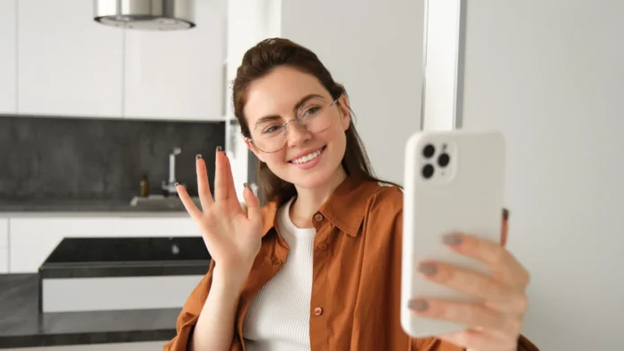 Portrait of stylish beautiful woman at home, video chats on smartphone, connects to online meeting from her living room, lifestyle social media blogger records a video on mobile phone. Portrait of stylish beautiful woman at home, video chats on smartphone, connects to online meeting from her living room, lifestyle social media blogger records a video on mobile phone.